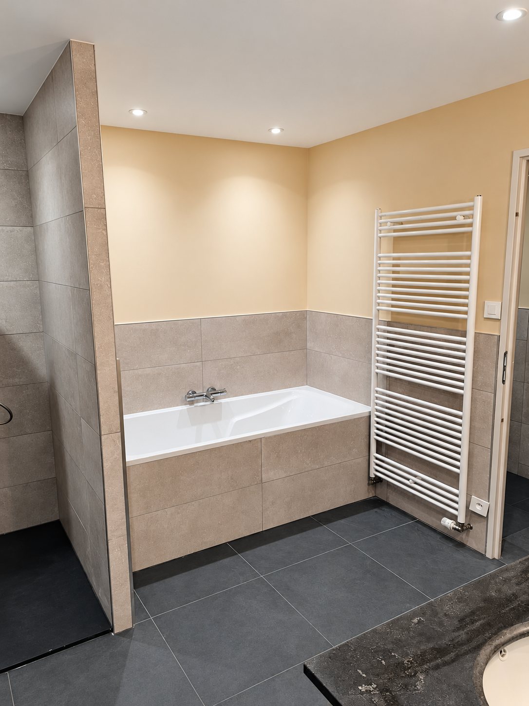 Salle de bain rénovée avec une baignoire encastrée, un carrelage beige et gris, une douche à l'italienne et un radiateur sèche-serviettes blanc.